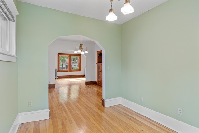 2505 Pleasant Ave, Minneapolis, MN 55404 - unfurnished room featuring a chandelier, arched walkways, light wood finished floors, baseboards, and radiator heating unit