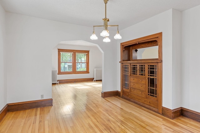 2505 Pleasant Ave, Minneapolis, MN 55404 - spare room with radiator heating unit, arched walkways, wood-type flooring, and baseboards