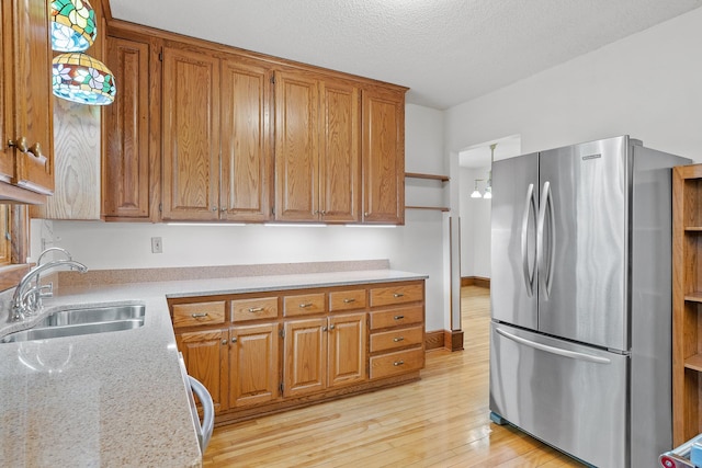 2505 Pleasant Ave, Minneapolis, MN 55404 - kitchen featuring freestanding refrigerator, a sink, light wood-style floors, brown cabinets, and baseboards