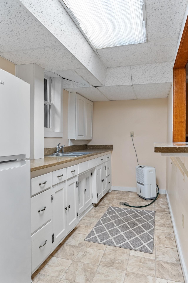 2505 Pleasant Ave, Minneapolis, MN 55404 - kitchen with freestanding refrigerator, white cabinets, baseboards, a sink, and a paneled ceiling