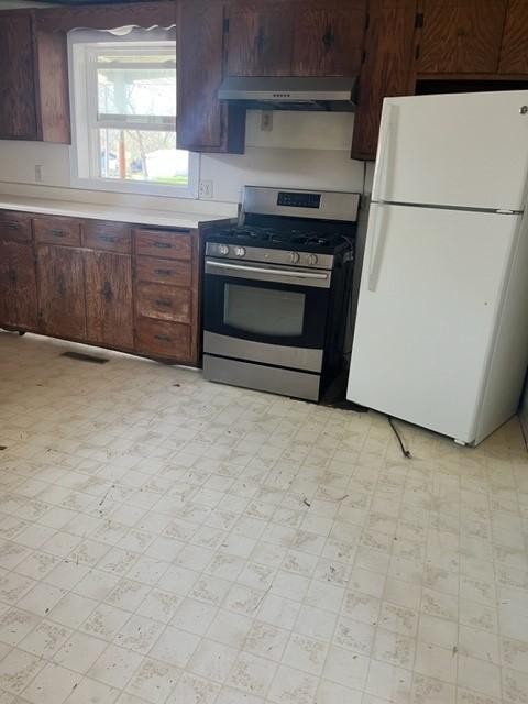 718 9th St N, Mountain Lake, MN 56159 - kitchen featuring freestanding refrigerator, stainless steel range with gas cooktop, under cabinet range hood, light countertops, and light floors