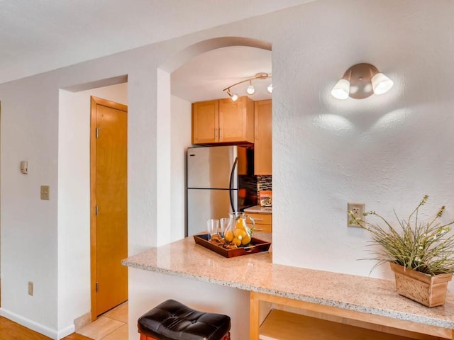 656 Ashland Ave Unit 11, Saint Paul, MN 55104 - kitchen featuring freestanding refrigerator, arched walkways, light stone counters, light tile patterned floors, and a kitchen breakfast bar