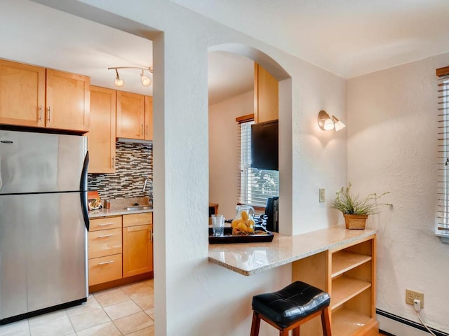 656 Ashland Ave Unit 11, Saint Paul, MN 55104 - kitchen with freestanding refrigerator, baseboard heating, decorative backsplash, arched walkways, and light stone countertops