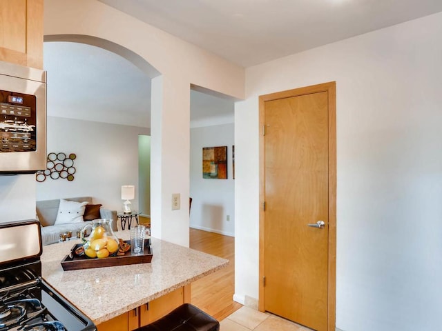 656 Ashland Ave Unit 11, Saint Paul, MN 55104 - kitchen featuring gas range, arched walkways, stainless steel microwave, light stone countertops, and light wood-type flooring