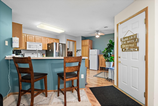 4645 Eagle Ridge Ln, Monticello, MN 55362 - kitchen with white appliances, a peninsula, a kitchen bar, ceiling fan, and light wood-style floors