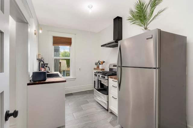 681 Dayton Ave, Saint Paul, MN 55104 - kitchen featuring appliances with stainless steel finishes, wall chimney range hood, white cabinetry, a sink, and baseboards