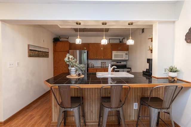 1269 Cleveland Ave N Unit 2B, Saint Paul, MN 55108 - kitchen featuring appliances with stainless steel finishes, brown cabinets, a sink, and a kitchen breakfast bar