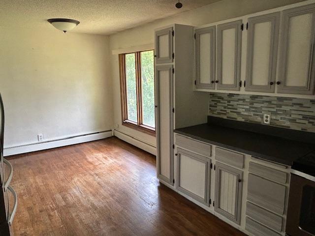 601 1st Ave, Grand Rapids, MN 55744 - kitchen featuring dark countertops, tasteful backsplash, dark wood-style floors, a baseboard radiator, and a textured ceiling