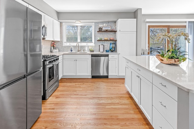 7136 145th St W, Apple Valley, MN 55124 - kitchen with stainless steel appliances, a sink, white cabinets, light wood finished floors, and decorative backsplash