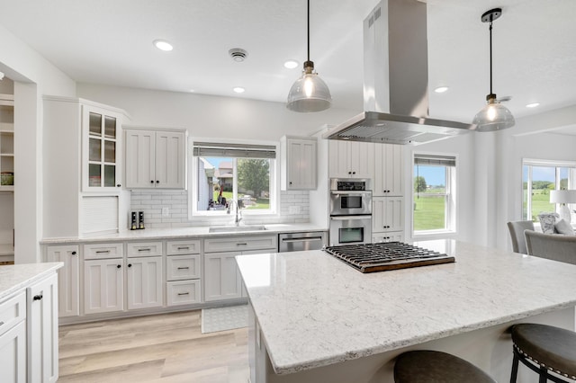 9867 Kahler Ave NE, Monticello, MN 55362 - kitchen featuring island exhaust hood, a sink, appliances with stainless steel finishes, light wood finished floors, and a kitchen bar