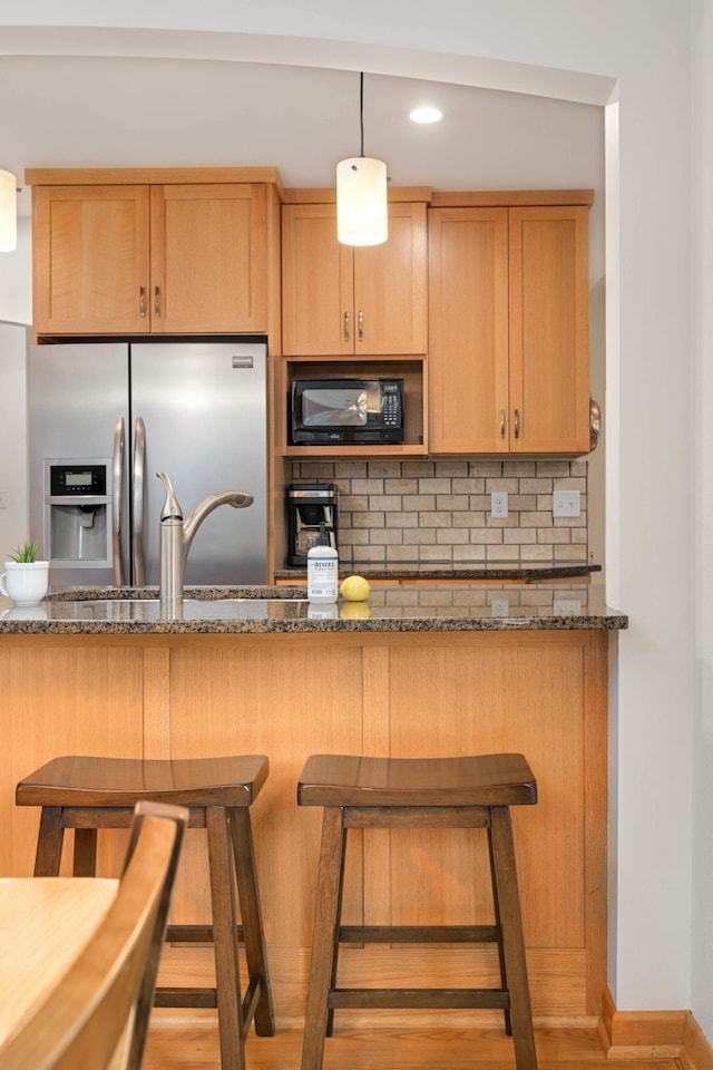 4313 Arthur St NE, Columbia Heights, MN 55421 - kitchen featuring stainless steel refrigerator with ice dispenser, black microwave, decorative backsplash, dark stone countertops, and a breakfast bar area