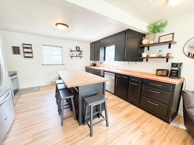 810 Division St, Elbow Lake, MN 56531 - kitchen featuring wooden counters, stainless steel appliances, dark cabinets, light wood finished floors, and a breakfast bar