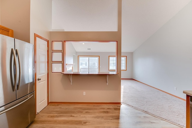 7539 Derby Ln, Shakopee, MN 55379 - kitchen featuring freestanding refrigerator, a breakfast bar, baseboards, vaulted ceiling, and light colored carpet