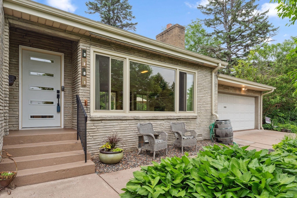 3201 Silver Lake Rd NE, Saint Anthony, MN 55418 - entrance to property with a chimney, concrete driveway, a garage, and stone siding