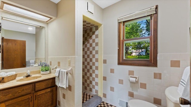9803 287th Ave NW, Zimmerman, MN 55398 - bathroom featuring tile walls, tiled shower, toilet, vanity, and a wainscoted wall
