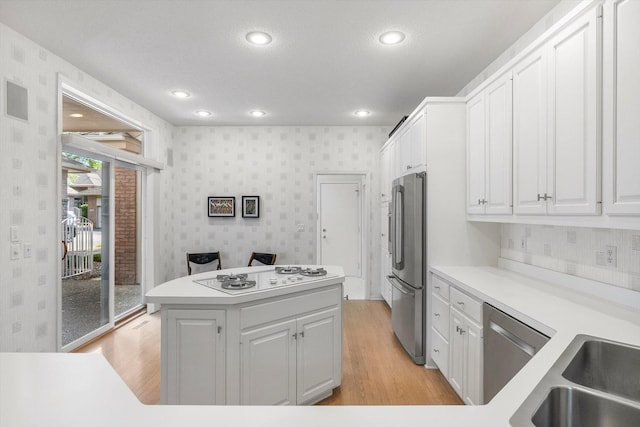 5555 70th St, Edina, MN 55439 - kitchen with appliances with stainless steel finishes, wallpapered walls, light wood-type flooring, white cabinets, and a kitchen island