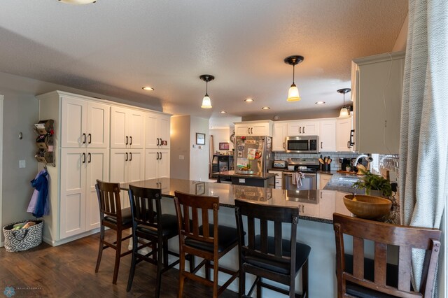 4408 Riverwood Dr N, Fargo, ND 58102 - kitchen with stainless steel appliances, a peninsula, dark wood-style floors, a breakfast bar area, and decorative light fixtures