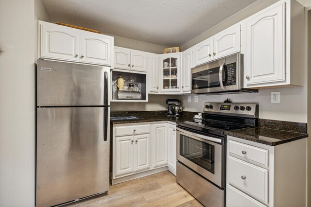 1198 Saint Clair Ave, Saint Paul, MN 55105 - kitchen featuring stainless steel appliances, white cabinetry, light wood-style flooring, glass insert cabinets, and a textured ceiling