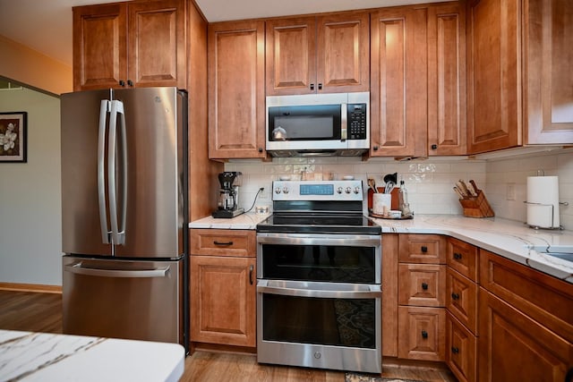 206 Skyline Hts, Wabasha, MN 55981 - kitchen featuring appliances with stainless steel finishes, brown cabinets, tasteful backsplash, light stone counters, and wood finished floors