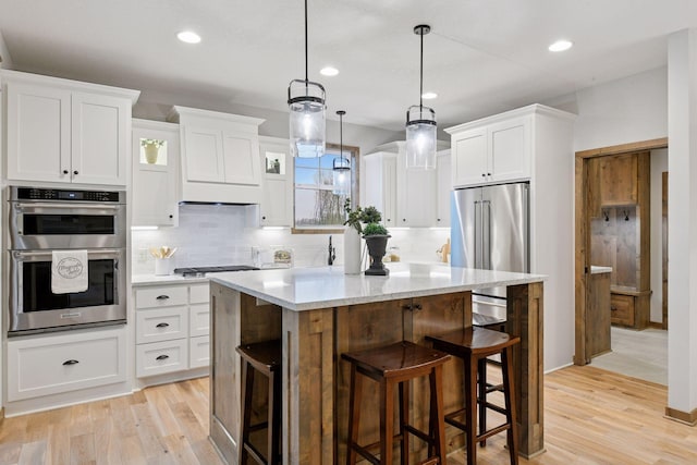 1843 Campfire Dr E, Waconia, MN 55387 - kitchen with appliances with stainless steel finishes, a kitchen bar, a center island, white cabinetry, and light wood finished floors