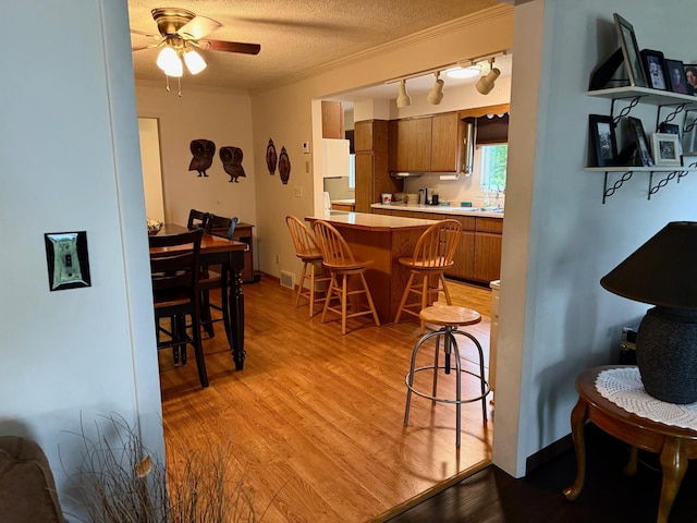 30055 Shore Dr, Pengilly, MN 55775 - kitchen featuring brown cabinetry, a breakfast bar, ceiling fan, light wood-style flooring, and a peninsula