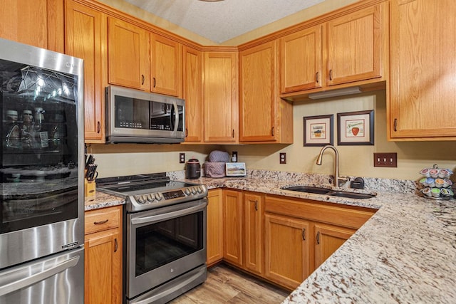 513 2nd Ave SW, Lonsdale, MN 55046 - kitchen featuring appliances with stainless steel finishes, a sink, light wood-type flooring, and light stone counters