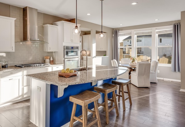 10329 Kentucky Ave N, Brooklyn Park, MN 55445 - kitchen featuring wall chimney exhaust hood, backsplash, white cabinets, hardwood / wood-style floors, and a kitchen bar