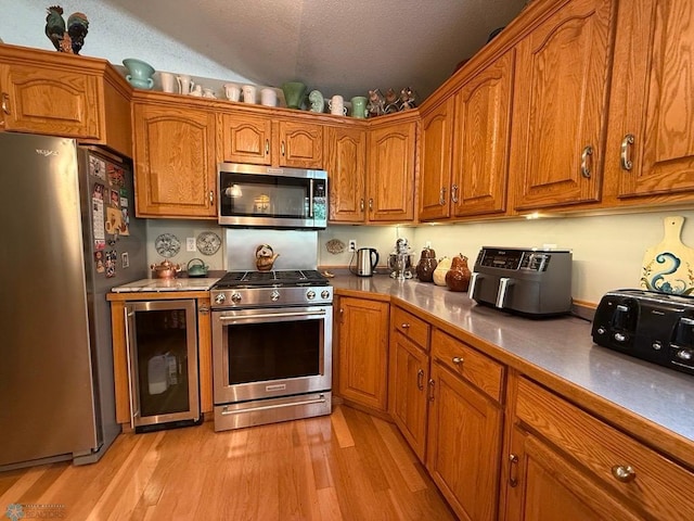 521 Kroshus Dr, Dilworth, MN 56529 - kitchen featuring appliances with stainless steel finishes, wine cooler, brown cabinets, light wood-style floors, and a textured ceiling