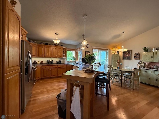 521 Kroshus Dr, Dilworth, MN 56529 - kitchen featuring stainless steel fridge with ice dispenser, light wood-type flooring, lofted ceiling, brown cabinets, and dark countertops