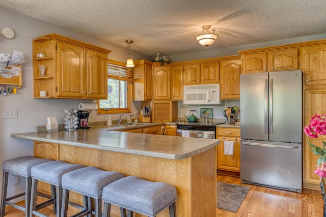 33240 Gary Dr, Grand Rapids, MN 55744 - kitchen featuring stainless steel appliances, a peninsula, a sink, a kitchen bar, and light wood-type flooring