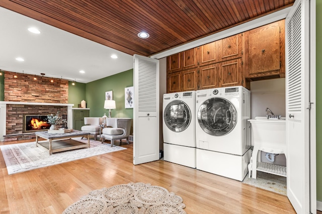 6521 Gleason Rd, Edina, MN 55439 - laundry room with light wood-style flooring, cabinet space, washing machine and dryer, a stone fireplace, and recessed lighting