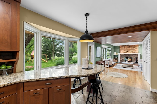 6521 Gleason Rd, Edina, MN 55439 - kitchen with a brick fireplace, hanging light fixtures, brown cabinets, light stone counters, and recessed lighting