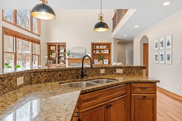 9256 Gateway Ln, Eden Prairie, MN 55347 - kitchen featuring a sink, light stone counters, light wood-type flooring, hanging light fixtures, and a towering ceiling