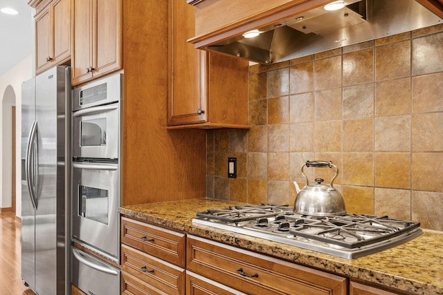9256 Gateway Ln, Eden Prairie, MN 55347 - kitchen featuring extractor fan, a warming drawer, stainless steel appliances, light stone counters, and brown cabinetry
