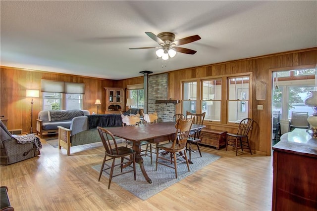 17174 59th Ave, Lafayette Twp, WI 54729 - dining area featuring wooden walls, a wood stove, ceiling fan, light wood-style floors, and a textured ceiling