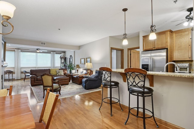 2670 Kelley Pkwy Unit 115, Orono, MN 55356 - kitchen featuring stainless steel fridge, ceiling fan, a kitchen breakfast bar, light wood finished floors, and light stone countertops