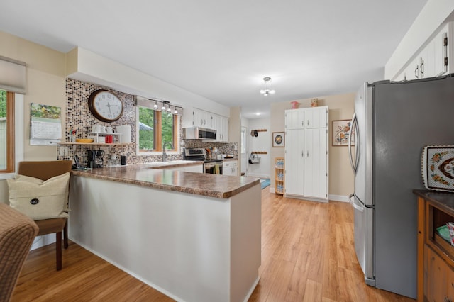 1501 Fraser Dr, Grand Rapids, MN 55744 - kitchen with appliances with stainless steel finishes, a peninsula, backsplash, and light wood-style floors