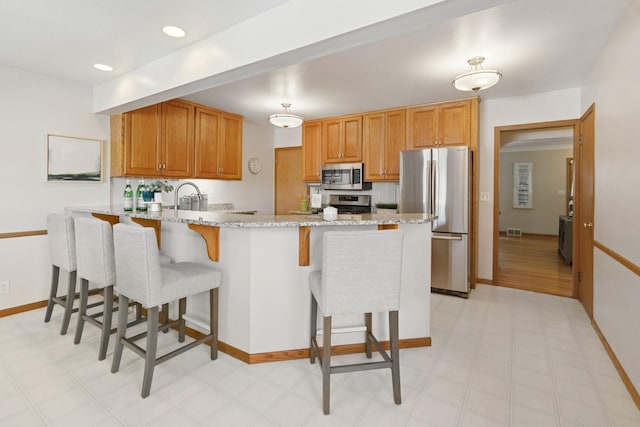 5409 Aldrich Ave S, Minneapolis, MN 55419 - kitchen featuring appliances with stainless steel finishes, a peninsula, a kitchen bar, and light stone counters