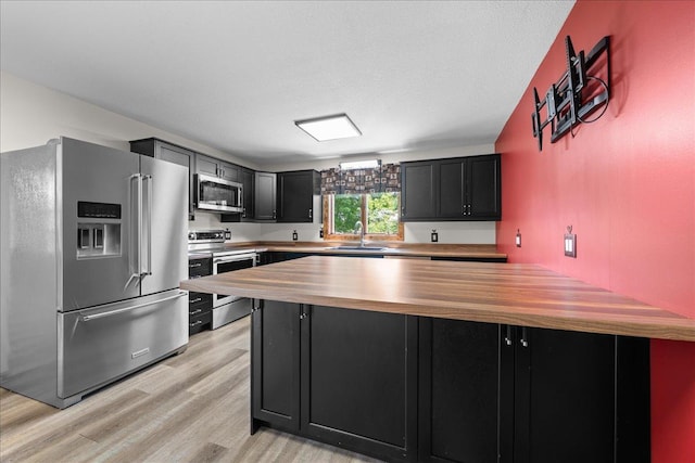 1334 105th Ave, Amery, WI 54001 - kitchen with stainless steel appliances, wooden counters, a sink, dark cabinetry, and light wood-style flooring