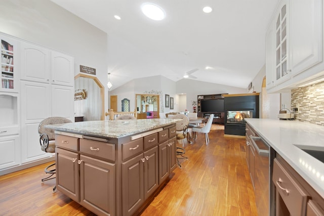 22946 185th St NW, Orrock Twp, MN 55309 - kitchen with light wood finished floors, white cabinets, vaulted ceiling, glass insert cabinets, and a multi sided fireplace