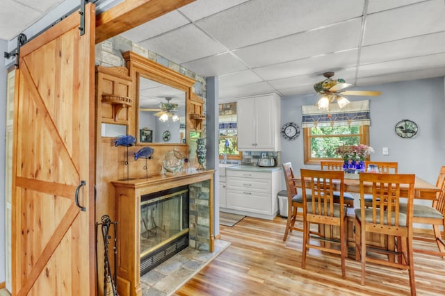 45909 Lands End Rd, Vergas, MN 56587 - dining area featuring ceiling fan, a drop ceiling, a barn door, light wood-type flooring, and a fireplace with flush hearth