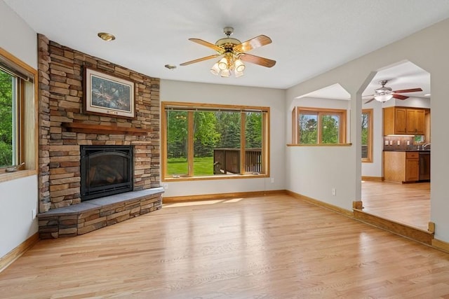 17575 Xenia St NW, Andover, MN 55304 - unfurnished living room featuring a ceiling fan, a stone fireplace, light wood-style flooring, and baseboards