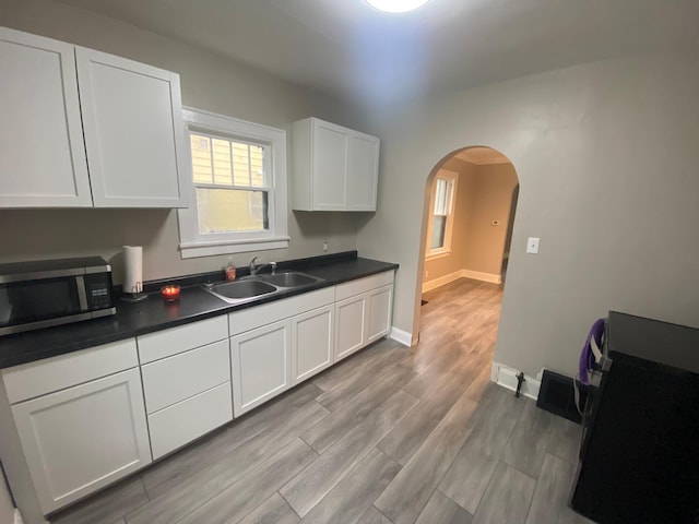 1138 6th Ave SE, Rochester, MN 55904 - kitchen featuring stainless steel microwave, arched walkways, dark countertops, white cabinets, and light wood finished floors