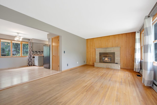 1121 Ramsey St W, Stillwater, MN 55082 - unfurnished living room featuring light wood-style floors, wooden walls, ceiling fan, a fireplace, and a baseboard radiator