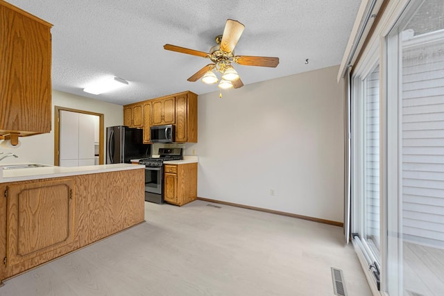 5214 148th St W, Apple Valley, MN 55124 - kitchen featuring appliances with stainless steel finishes, a textured ceiling, ceiling fan, a peninsula, and brown cabinetry