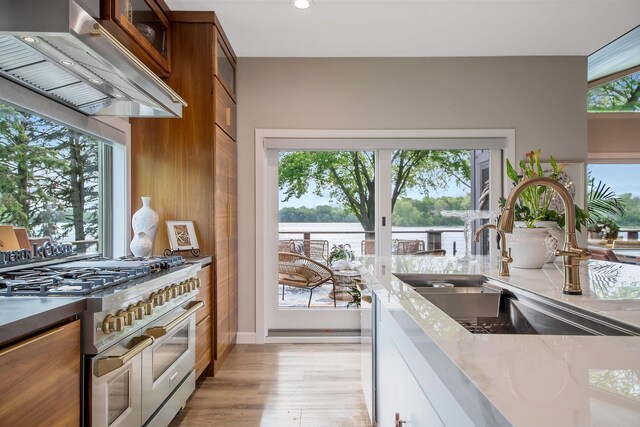 2311 Swan Dr, Mendota Heights, MN 55120 - kitchen with a sink, range with two ovens, wall chimney range hood, brown cabinetry, and glass insert cabinets