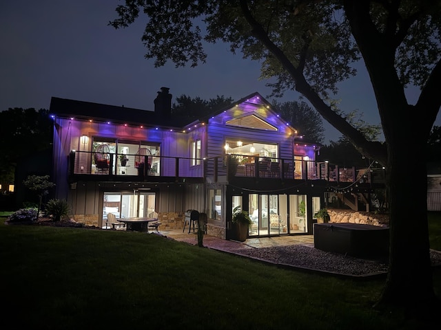 2311 Swan Dr, Mendota Heights, MN 55120 - back of house at night with a balcony, a lawn, a patio area, a chimney, and a hot tub