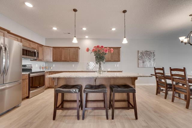 2605 Hanson Ave, Faribault, MN 55021 - kitchen with appliances with stainless steel finishes, light wood-style floors, backsplash, a kitchen breakfast bar, and a kitchen island