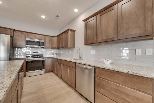 2605 Hanson Ave, Faribault, MN 55021 - kitchen featuring appliances with stainless steel finishes, a sink, light wood-style flooring, tasteful backsplash, and light stone countertops