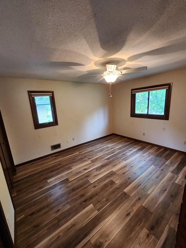 1180 Hathaway Ln NE, Fridley, MN 55432 - spare room with dark wood-style flooring, healthy amount of natural light, a textured ceiling, a ceiling fan, and baseboards